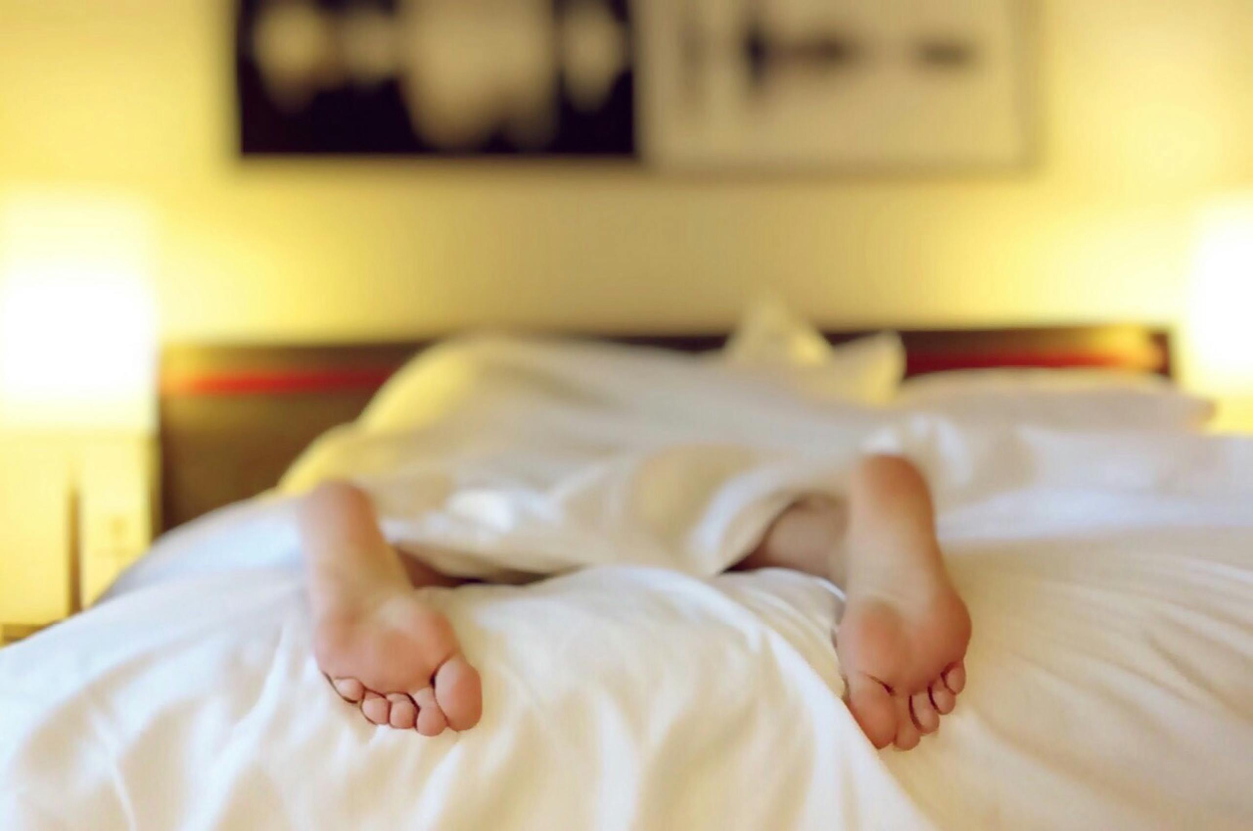 Person resting peacefully under soft white bedding in tranquil bedroom environment