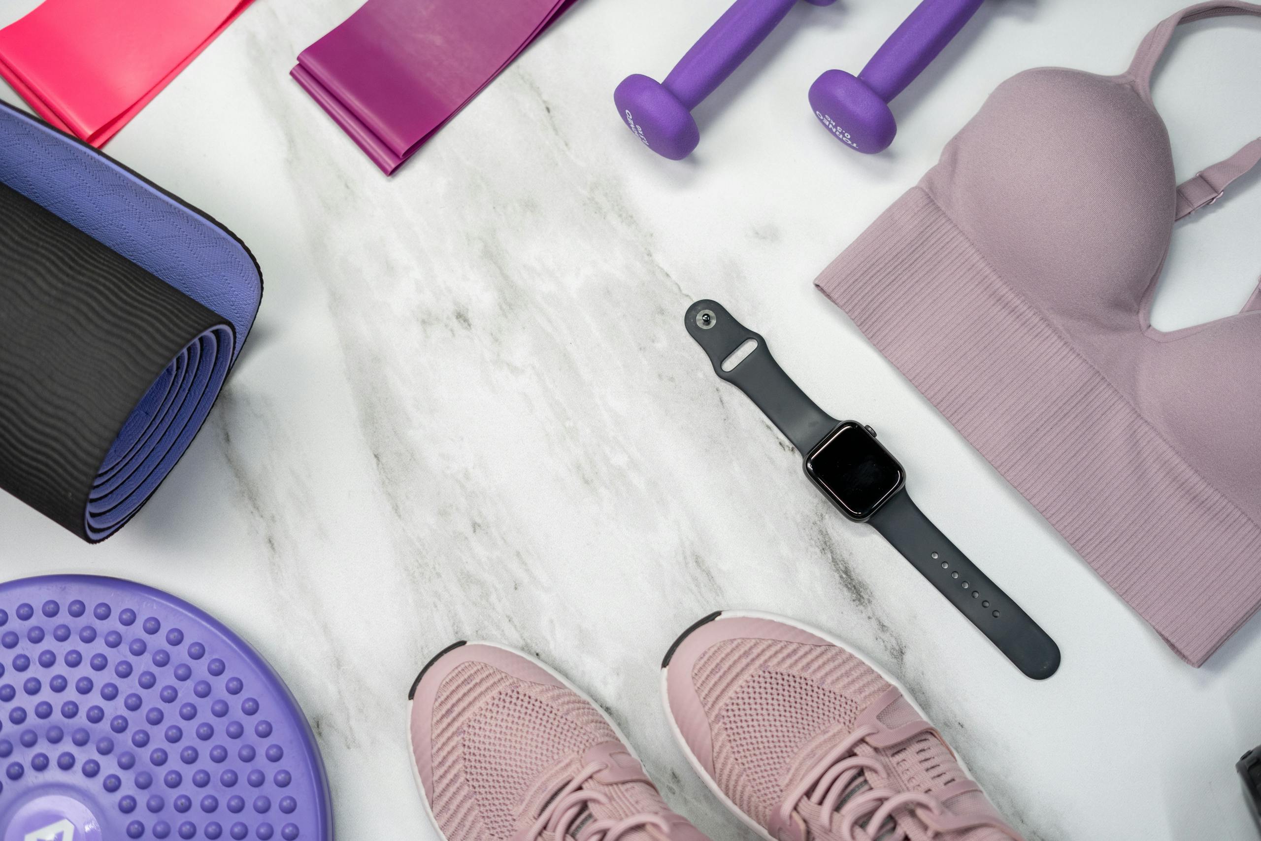 Fitness equipment flat lay with smartwatch dumbbells and yoga mat on clean marble surface
